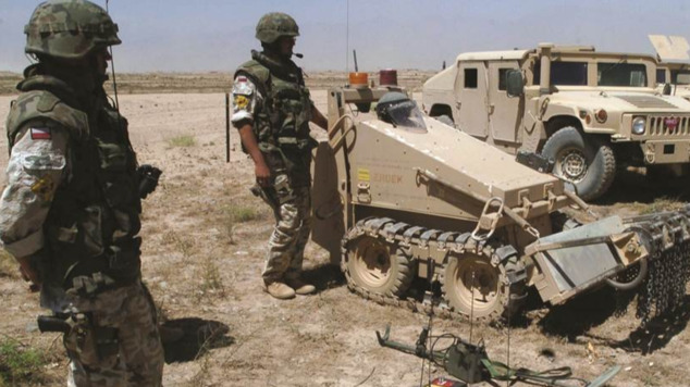 Dwaj żołnierze w pełnym umundurowaniu i ochronnych Dwaj żołnierze w pełnym umundurowaniu i ochronnych hełmach stoją przy robotach oczyszczających pola z min.