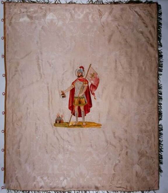 Sztandar z wizerunkiem św. Floriana. Mężczyzna w stroju rzymianina, w płaszczu i hełmnie na głowie i horągwią w jednej ręce, w drugiej trzyma naczynie z wodą, którą gasi pożar domu.
