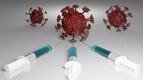 Trzy strzykawki leżą na stole skierowane w kierunku trzech kul, symbolizujących komórki wirusa