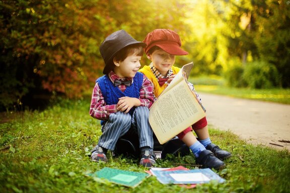 dwóch chłopców siedzi na skraju lasu i czyta książkę