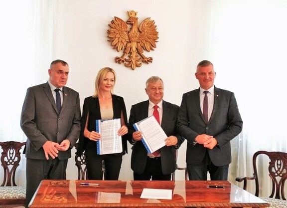 Przedstawiciele gminy Belsk Duży i samorządu Mazowsza stoją, pozując do zdjęcia. Dwie osoby trzymają egzemplarze podpisanej umowy