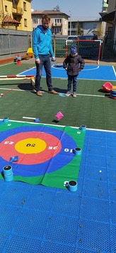 dziecko z nauczycielem stoją na podwórku szkolnym, przed nimi rozłożona jest kolorowa mata do gier