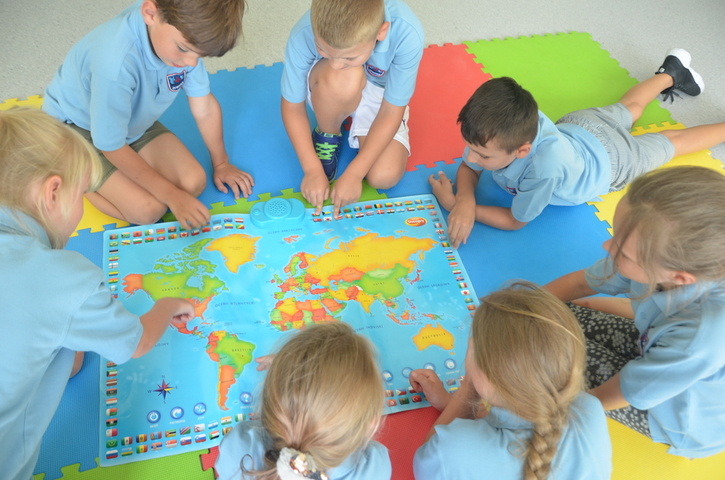 piątka dzieci w wieku szkolnym siedzi na podłodze wokół rozłożonej mapy świata