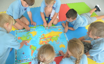 piątka dzieci w wieku szkolnym siedzi na podłodze wokół rozłożonej mapy świata