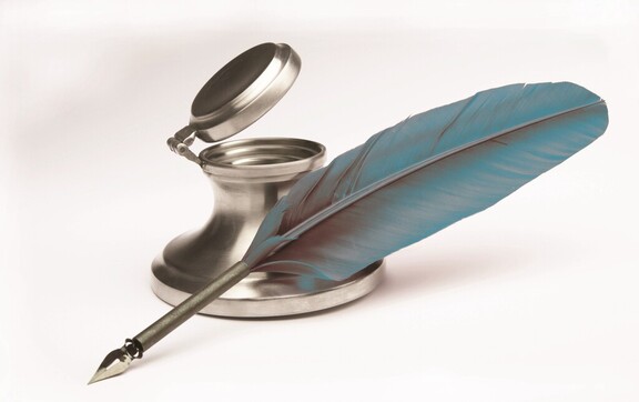 srebrny kałamarz z podniesionym wieczkiem, oparte o niego ptasie pióro, zaostrzone do pisania