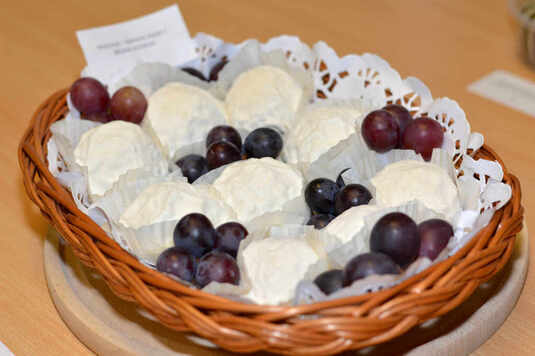Na wiklinowym koszyku leżą kulki białego sera poprzedzielane winogronami