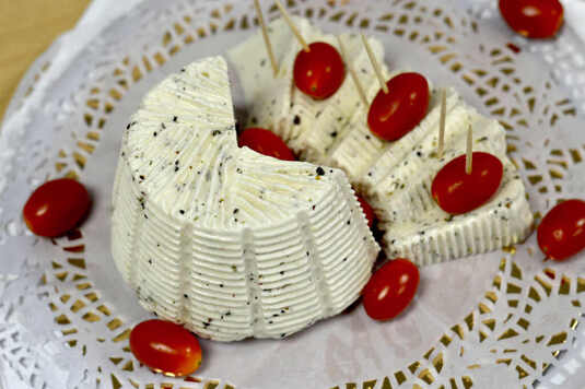 Biały ser z wyraźnie zaznaczonymi plamami od kozieradki w połowie podzielony jest na kawałki nadziane na wykałaczki z pomidorem