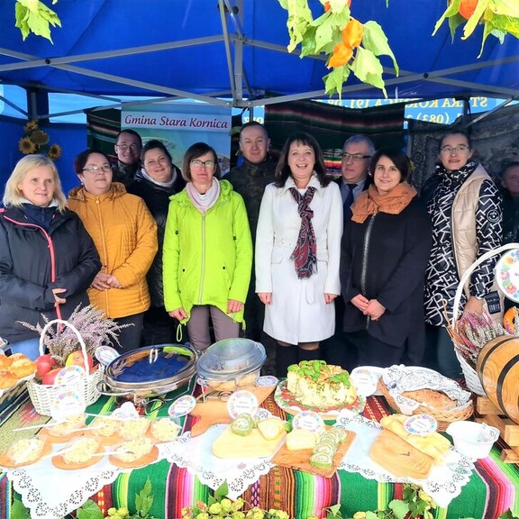 grupa uśmiechniętych kobiet stoi przed dużym stołem, na którym stoją liczne potrawy