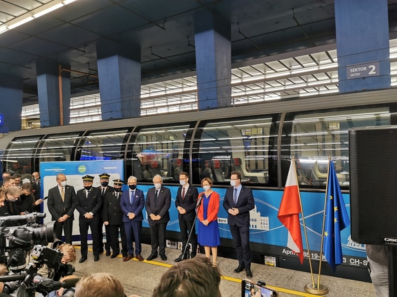 Przedstawiciele Unii Europejskiej, Samorządu Województwa Mazowieckiego oraz kolei stoją na peronie. ZA ich plecami stoi pociąg Connecting Europe