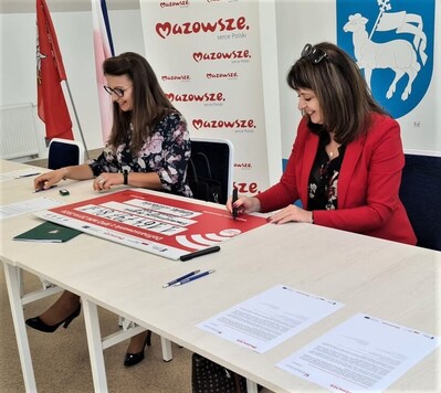 Dwie kobiety siedzą przy stole konferencyjnym i podpisują dokumenty.