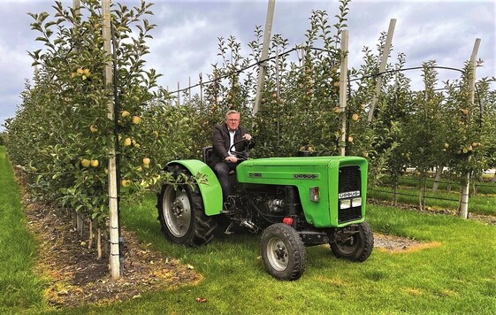 Mężczyzna na traktorze ursus na tle owocujących jabłoni