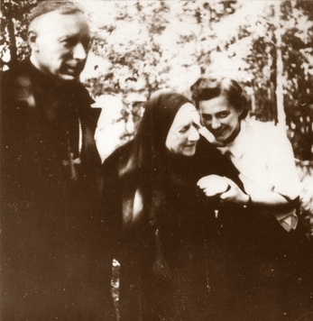 Zdjęcie archiwalne przedstawiające trzy osoby: od lewej ksiądz Stefan Wyszyński, pośrodku zakonnica matka Czacka podtrzymywana pod rękę przez uśmiechniętą kobietę, która się nad nią pochyla.