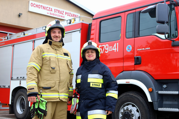 Mężczyzna i kobieta w mundurach strażakich na tle samochodu strażackiego