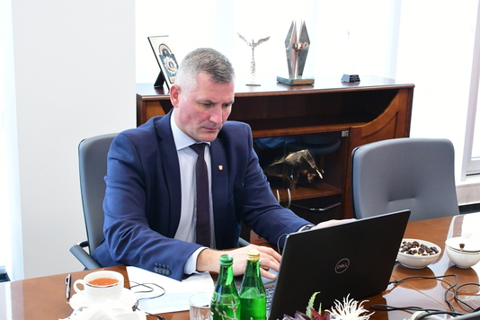 Wicemarszałek Rafał Rajkowski siedzi przy stole przed otwartym laptopem. Dłonie ma na klawiaturze