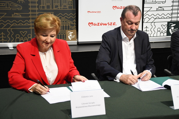 Elżbieta Lanc i Wiesław Raboszuk siedzą obok siebie przy stole i podpisują dokumenty