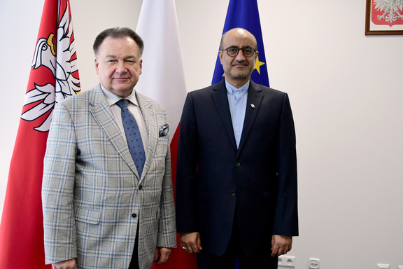 Marszałek i przedstawiciel ambasady Iranu pozują do zdjęcia na tle flag UE, Polski i mazowsza