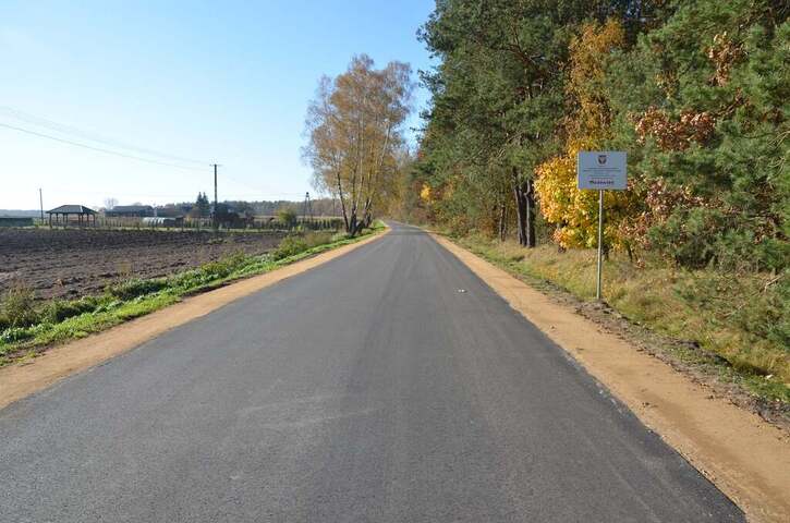 Nowy asfalt na drodze. Po prawej stronie drogi rośnie las, po lewej widać pole