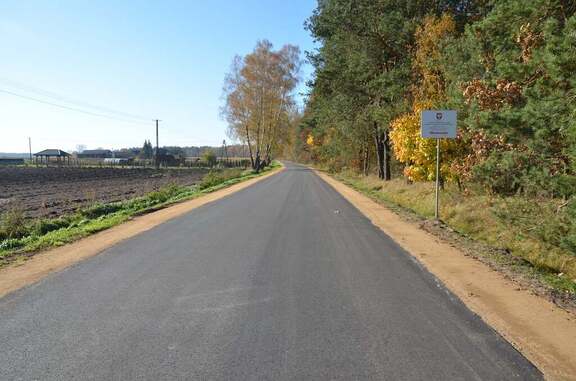 Nowy asfalt na drodze. Po prawej stronie drogi rośnie las, po lewej widać pole