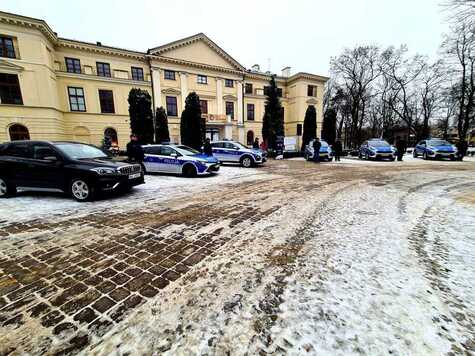 Przed zabytkowym budynkiem pałacu Dernałowiczów stoją ustawione w półkolu zakupione pojazdy. Przy każdym stoi policjant