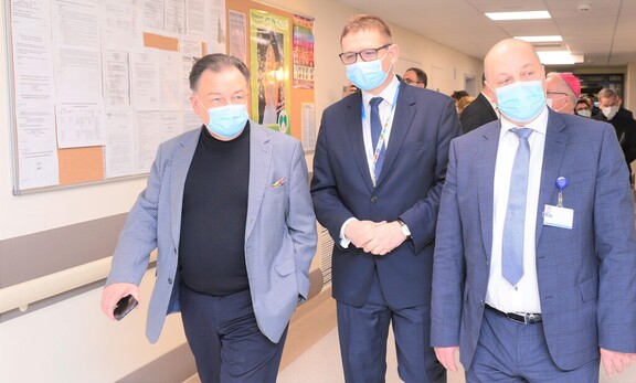 Trzech mężczyzn w maseczkach na twarzy idą obok siebie korytarzem szpitalnym