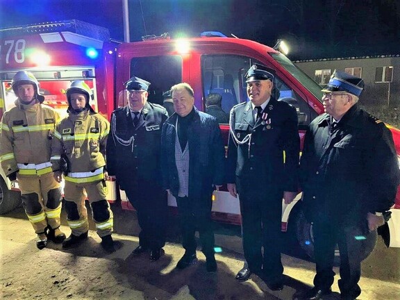 Pięciu mężczyzn stoi przed wozem strażackim