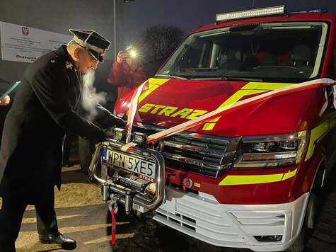 Strażak rozwiązuje wstęgę zawiązaną na masce nowego samochodu strażckiego
