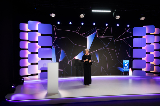 Kobieta w długiej sukni stoi na scenie z mikrofonem w ręku