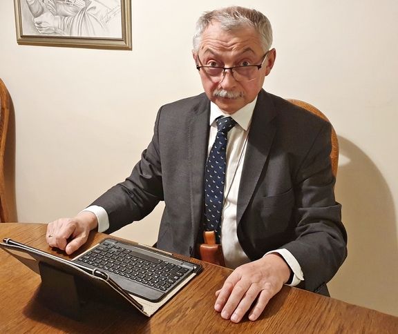 Przewodniczący Skolimowski siedzi przy biurku przed otwartym laptopem. Patrzy się w kamerę