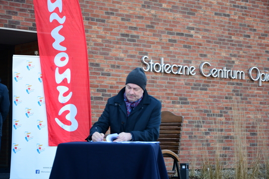 Wicemarszałek Wiesław Raboszuk podpisuje umowę, w tle flaga Mazowsze