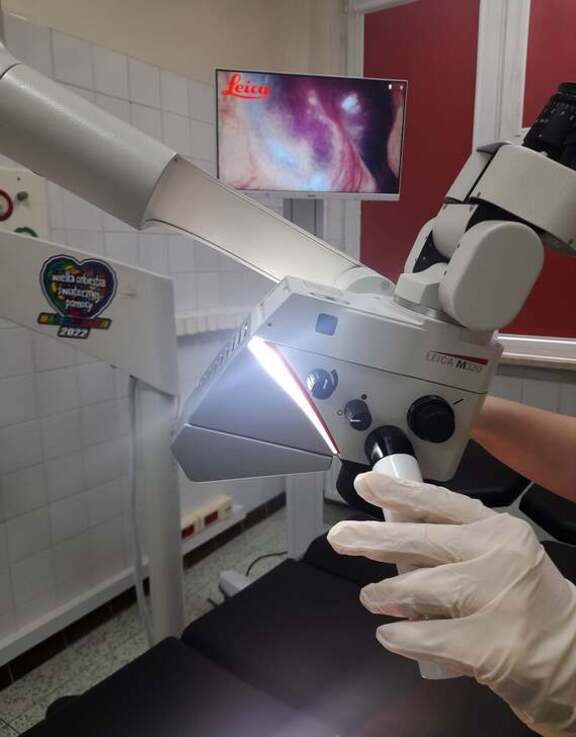 Ręka w rękawiczce diagnostycznej steruje aparaturą, obok jest monitor z wyświetlanym obrazem badanego obszaru oka