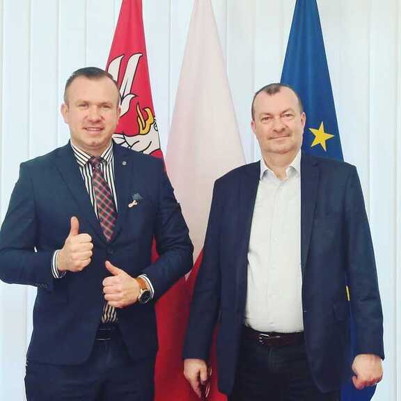 Wicemarszałek Raboszuk pozuje do zdjęcia z wójtem Załusek na tle flagi Mazowsza i UE
