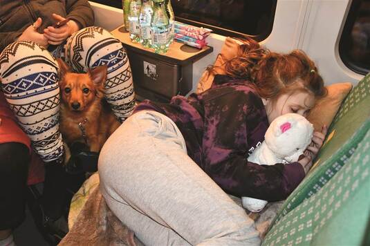 Skulona dziewczynka przytula maskotkę i śpi na fotelach w pociągu.