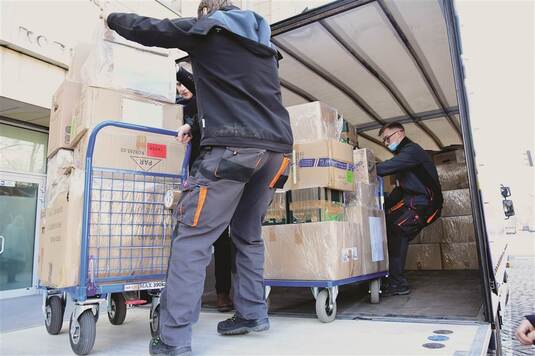 Mężczyźni transportują na specjalnych wózkach do samochodu dostawczego zapakowane  dary.