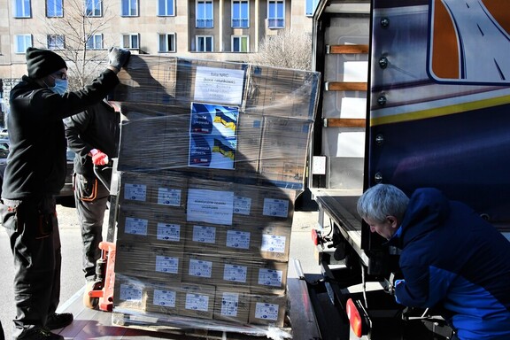 Trzech mężczyzn pakuje do otwartej ciężarówki wielką paletę pudeł, na których jest napisane "obwód lwowski" oraz "opaski uciskowe".