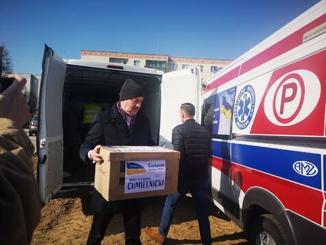 Mężczyzna w czapce przenosi pudło z darami od Mazowsza dla Ukrainy, z samochodu dostawczego do karetki