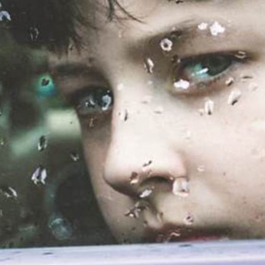 Twarz dziecka wyglądającego przez okno pociągu. Na szybie krople deszczu