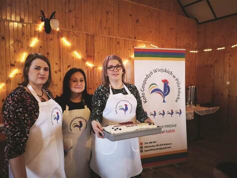 Trzy młode kobiety w fartuchach kuchennych z logotypem koła gospodyń wiejskich