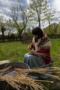 Zdjęcie przedstawia kobietę przygotowującą naczynie ze słomy.
