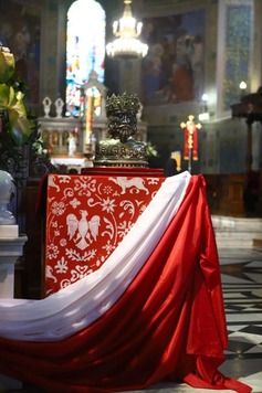 Na cokole zakrytym czerwonym obrusem i flagą Polski stoi popiersie świętego, zrobione ze srebra i drogich kamieni w koronie
