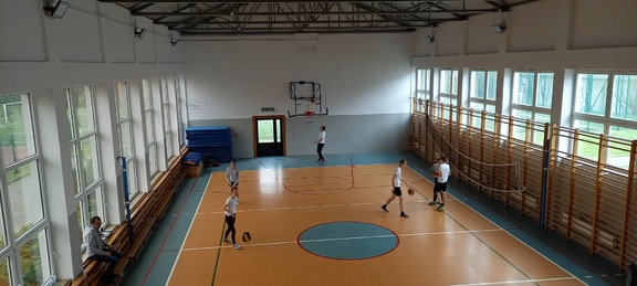 Na sali gimnastycznej kilku uczniów gra w koszykówkę