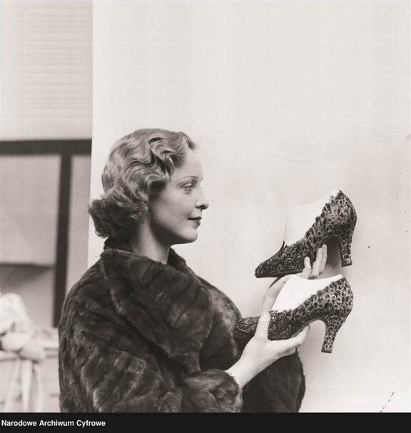 Elegancko ubrana kobieta trzyma w dłoniach parę bardzo pięknych, ozdabianych szpilek. Zdjęcie z lat 30. XX w.