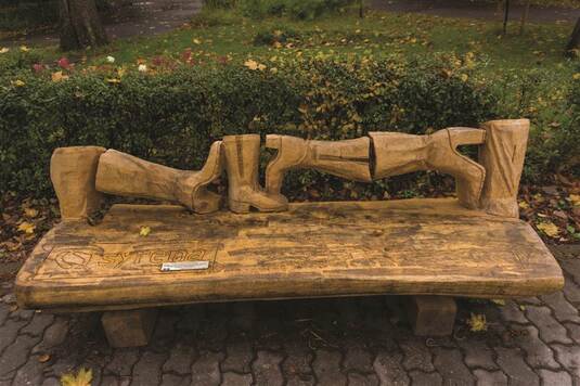 Drewniana ławka, której oparcie ma kształt damskich kozaków ułożonych w rzędzie