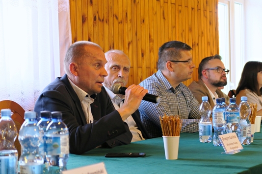 Przy stole siedzą samorządowcy powiatów grodziskiego i pruszkowskiego. Na pierwszym planie siedzi wicestarosta powiatu pruszkowskiego Grzegorz Kamiński, który trzyma w ręku mikrofon.