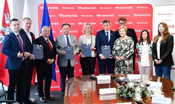 kilku uczestników podpisania umowy na budowę tunelu w Sulejówku na Mazowszu stoi obok siebie, w tle czerwony baner z białymi napisami Mazowsze serce Polski