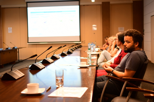 Grupa osób siedzi przy stole konferencyjnym, w tle prezentacja na ekranie