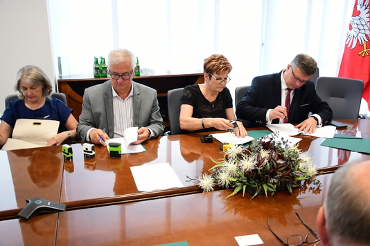 Grupa osób siedzi przy stole i podpisuje umowy