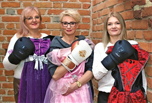 Trzy uśmiechnięte kobiety w rękawicach bokserskich trzymają sukienki.