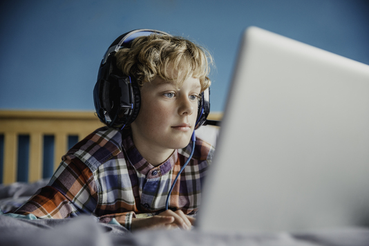 Chłopiec w słuchawkach na uszach patrzy w ekran laptopa