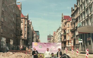 Członkowie zespołu Muchy pozują do zdjęcia na remontowanej ulicy na tle baneru z różowym niebem