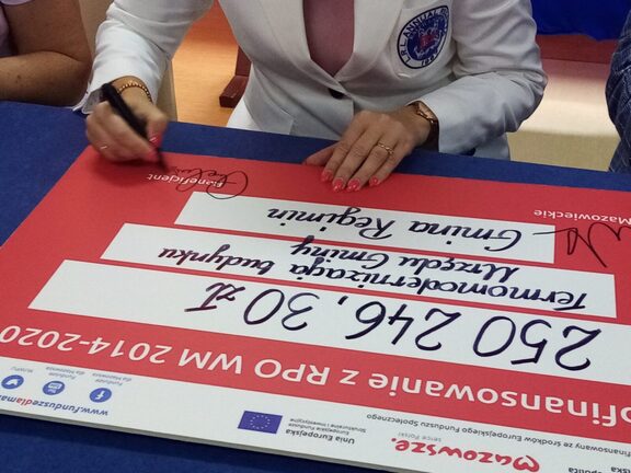 kobieta podpisuje symboliczny czek opiewający na kwotę 250 tys. zł na realizację inwestycji w gminie Regimin